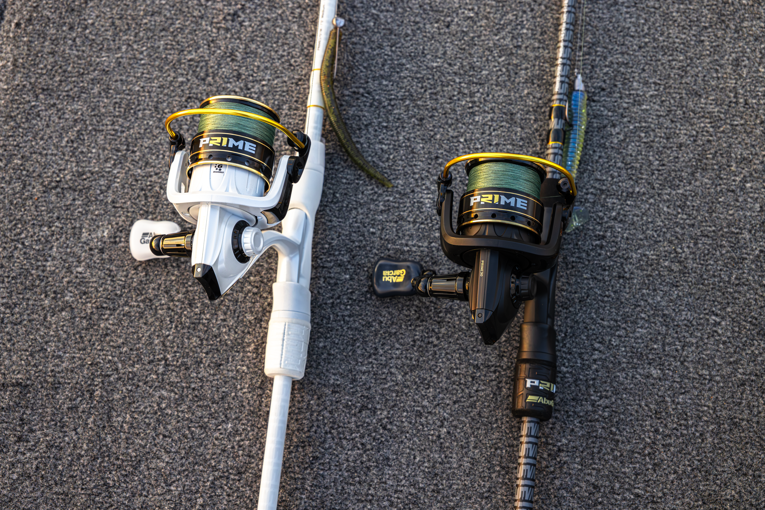 Two Abu Garcia + PRIME21 Collaboration Spinning Combos laying flat on pavement, one black & one white. 